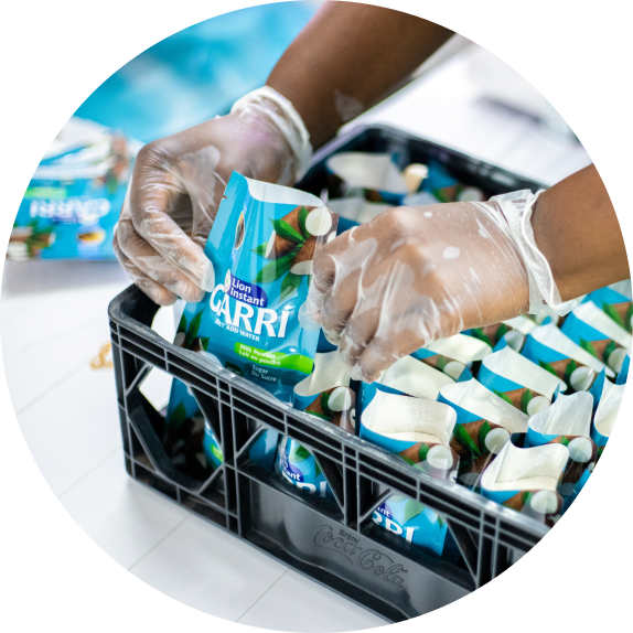 A person wearing protective gloves packs sachets of instant cassava flour (gari) into a plastic crate.